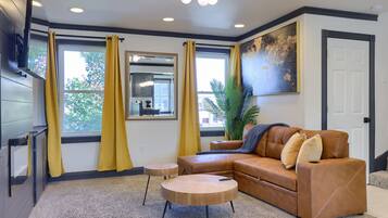 A modern living room with a brown leather sofa, two round wooden coffee tables, and yellow curtains.