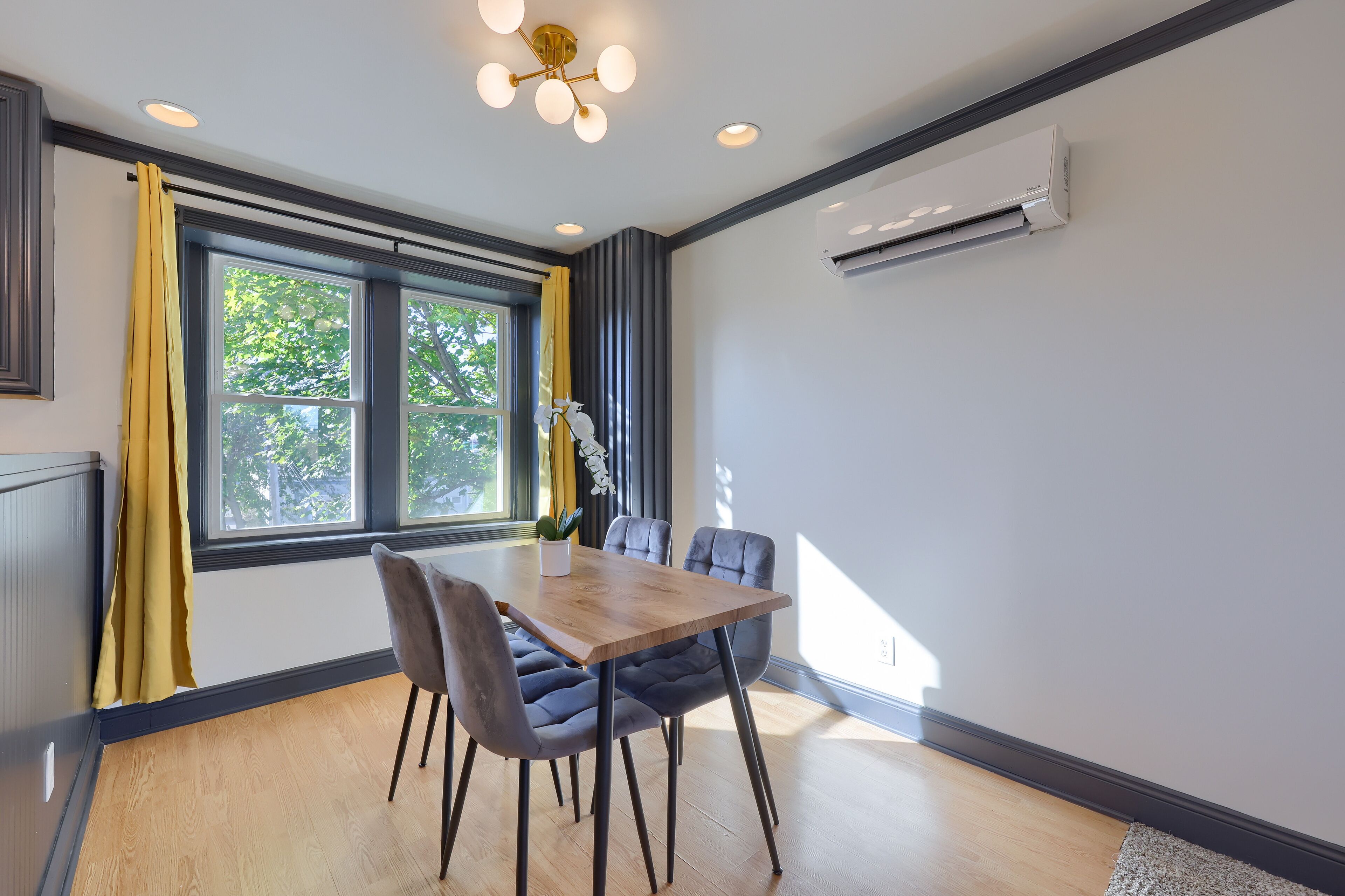 A modern dining area with a wooden table and chairs, a potted plant, and a window with curtains.