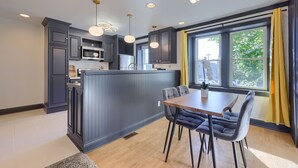 A modern kitchen with dark cabinetry, a central island, and a dining area with a table and chairs. - Modern Downtown Lancaster Apt – Walk to Train & Amtrak (Lancaster)