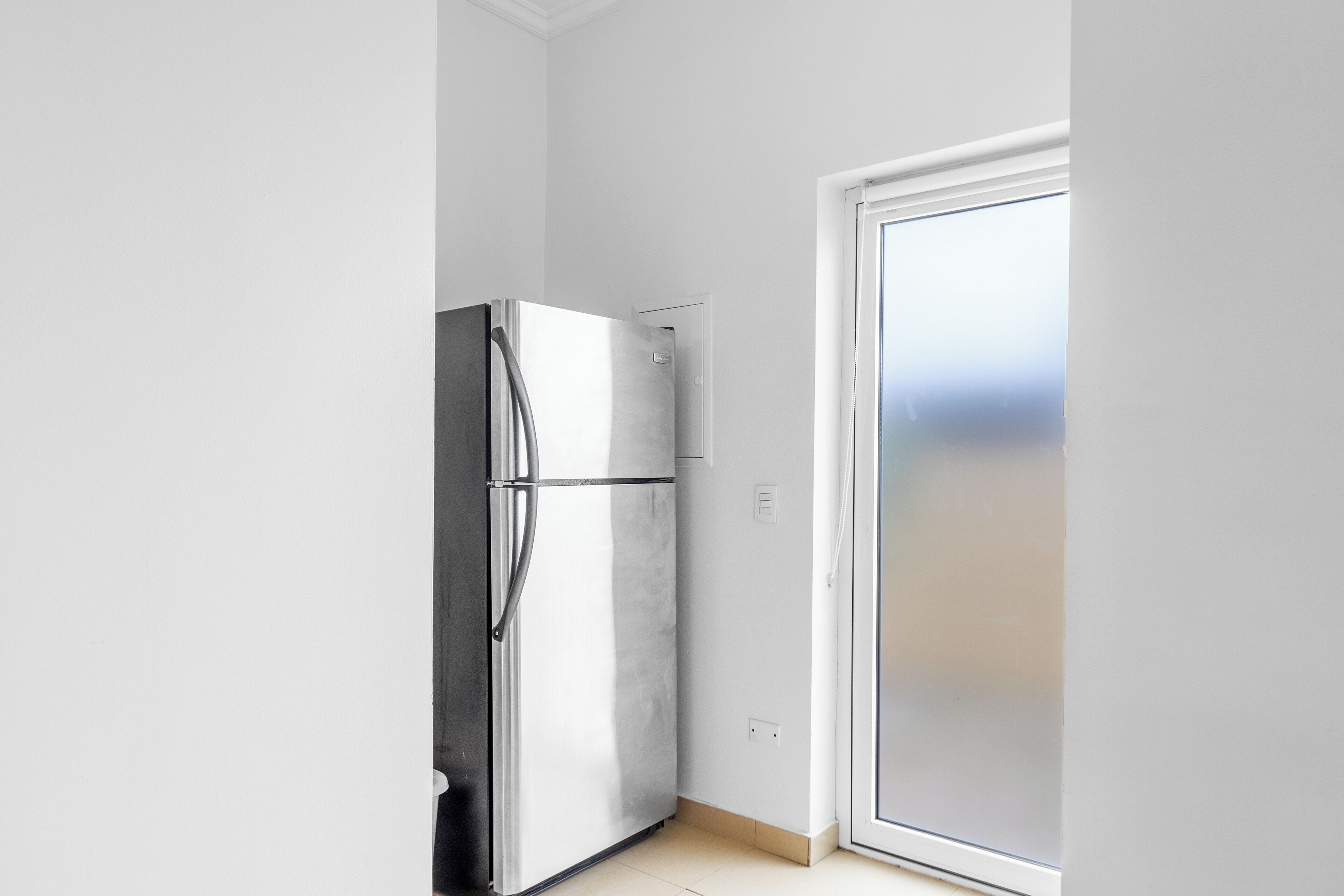 A kitchen with a stainless steel refrigerator, a sliding glass door, and a light-colored floor.