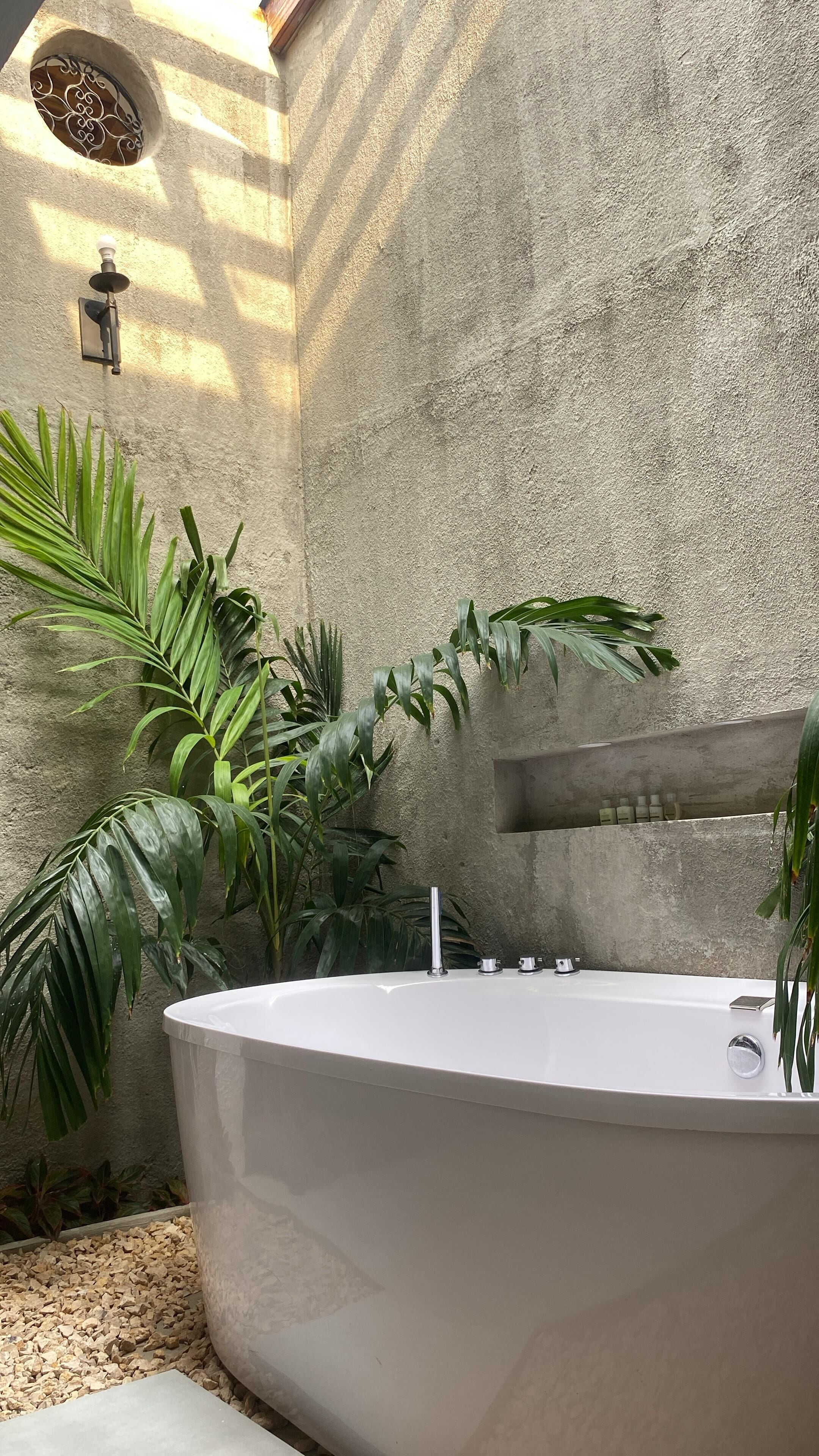 Un espace spa doté d’une baignoire sur pied, entouré de plantes tropicales et d’un mur en pierre à la texture particulière.