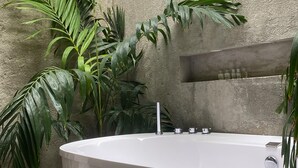 A spa area with a freestanding bathtub, surrounded by tropical plants and a textured stone wall.