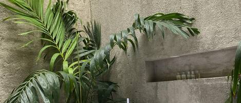 A spa area with a freestanding bathtub, surrounded by tropical plants and a textured stone wall.