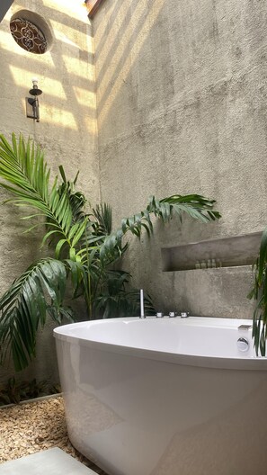 A spa area with a freestanding bathtub, surrounded by tropical plants and a textured stone wall.