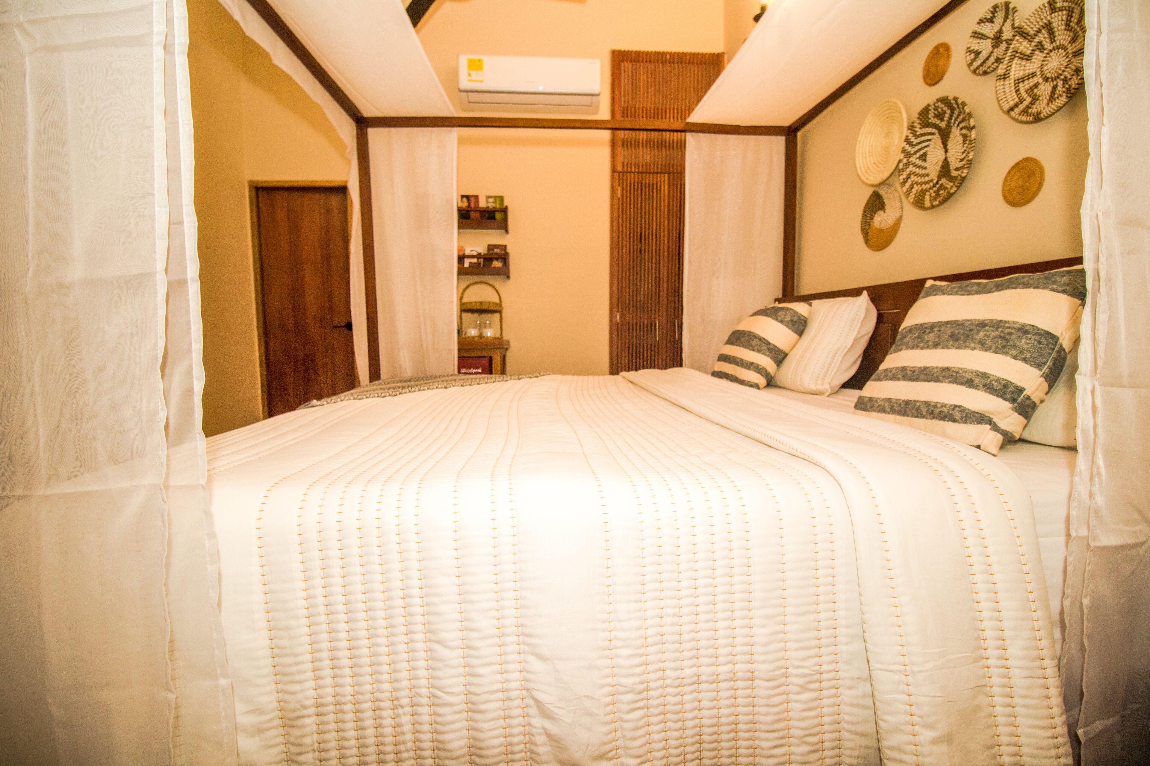 A neatly made bed with a quilted cover, a wooden headboard, and a wall with woven baskets.