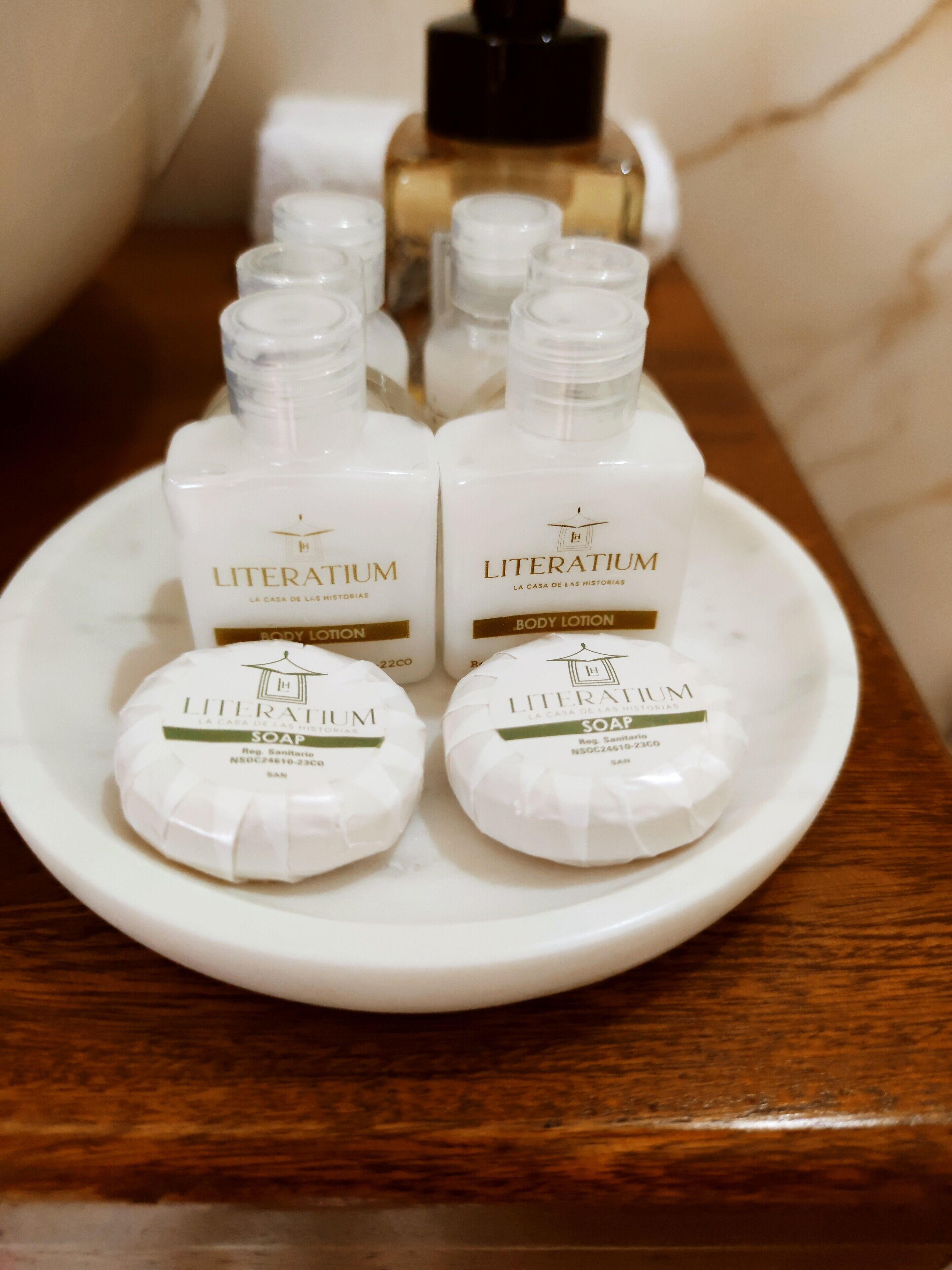 Un plato blanco con cuatro botellas de crema corporal Literarium y dos botellas de jabón Literarium sobre una superficie de madera.