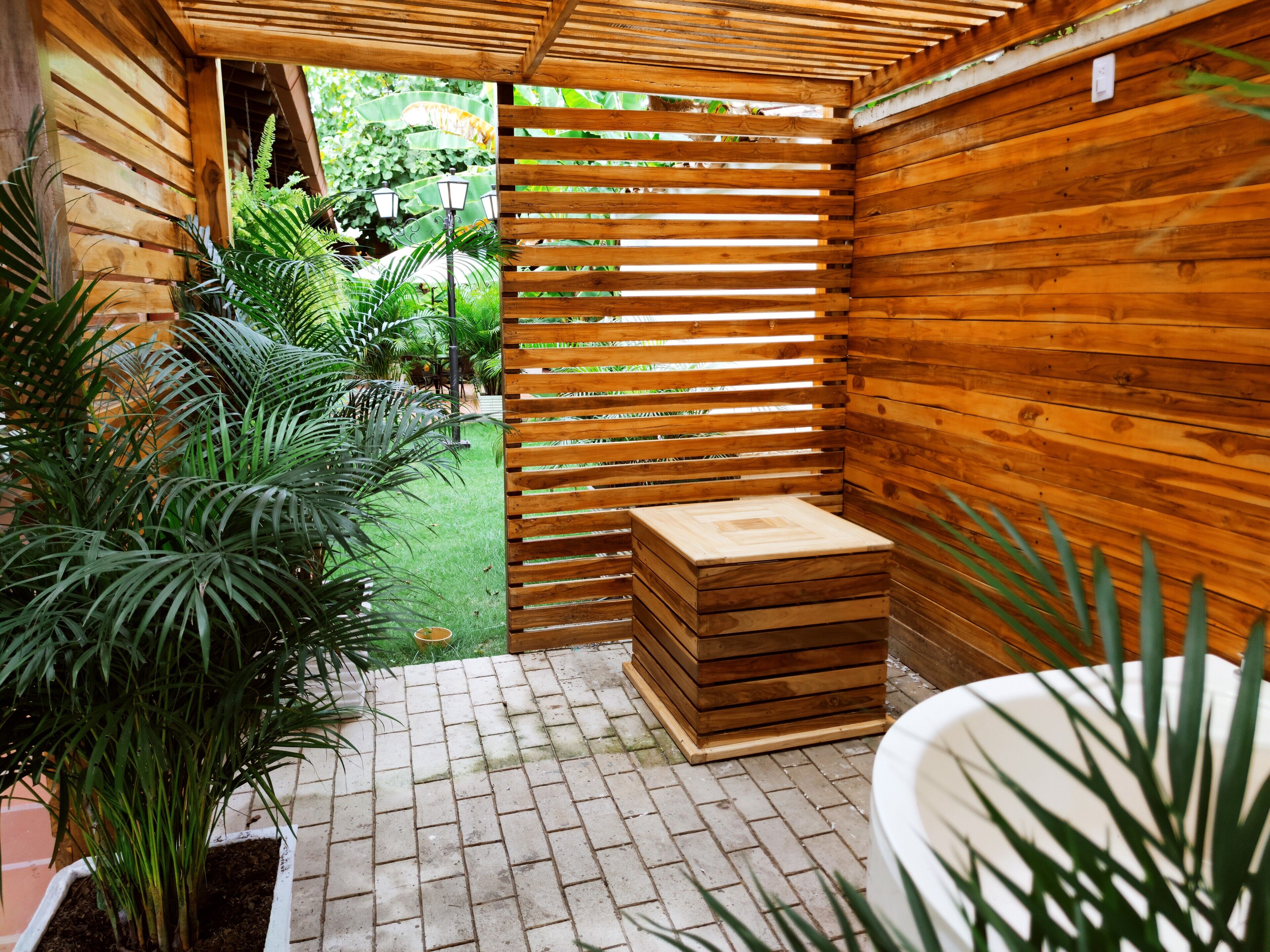 A wooden outdoor shower area with a bench and potted plants.