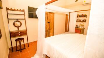 A bedroom with a bed, a wooden desk, a chair, a mirror, and a wardrobe.