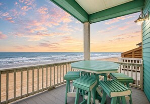Eine Holzterrasse mit Tisch und Stühlen mit Blick auf einen Strand.