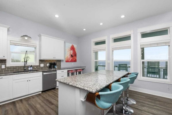 A modern kitchen with white cabinets, a granite countertop, and a bar area with blue chairs. - Pet Friendly Beachfront with Heated Pool & Fire Pit (Crystal Beach)