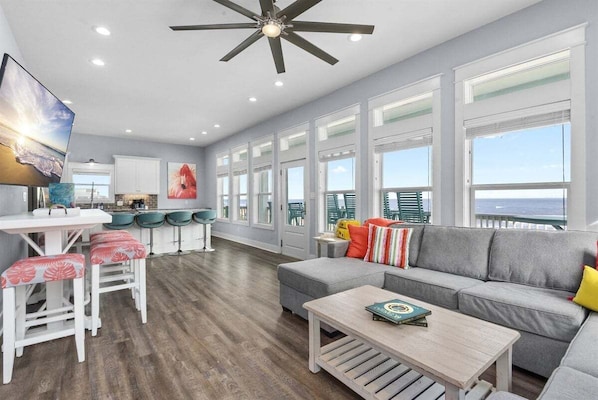 A spacious living area with a gray sofa, a coffee table, and a dining area with a white table and red chairs. - Pet Friendly Beachfront with Heated Pool & Fire Pit (Crystal Beach)