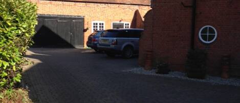 Une allée pavée mène à un bâtiment en briques doté d’un garage et où est garée une voiture.