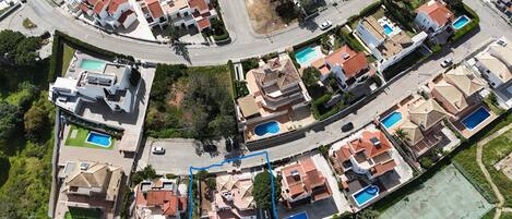An aerial view of a residential area with houses, roads, and swimming pools.