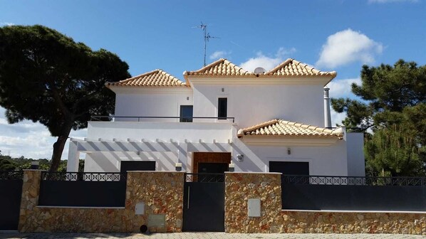 Una casa moderna de dos pisos con fachada blanca, tejas de arcilla y entrada con muro de piedra.