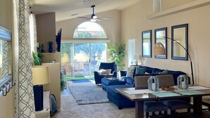 A spacious living room with a large window, a ceiling fan, and a dining area with a table and chairs. - Snowbird Winter Villa (Bullhead City)