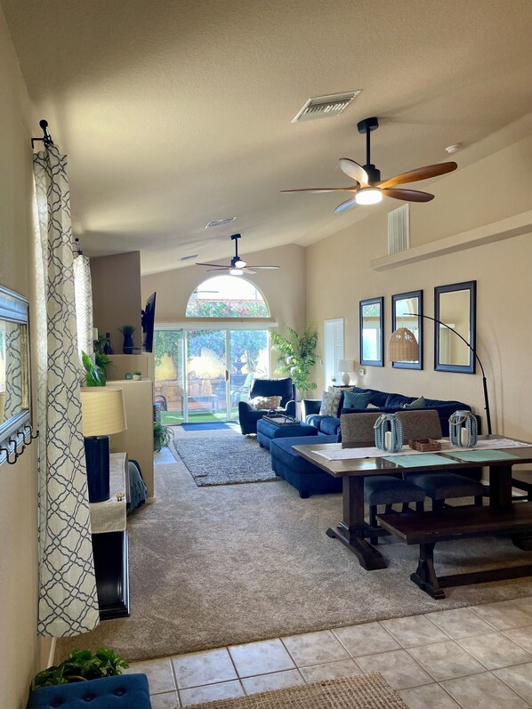 A spacious living room with a large window, a ceiling fan, and a dining area with a table and chairs.