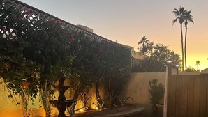 A courtyard with a stone fountain, a wooden fence, and a wall covered in climbing plants. - Snowbird Winter Villa (Bullhead City)