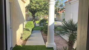 A covered patio with a concrete pathway, white columns, and a small lawn area. - Snowbird Winter Villa (Bullhead City)