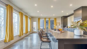 Una cocina moderna con una isla central, taburetes de bar y un amplio ventanal con cortinas amarillas.