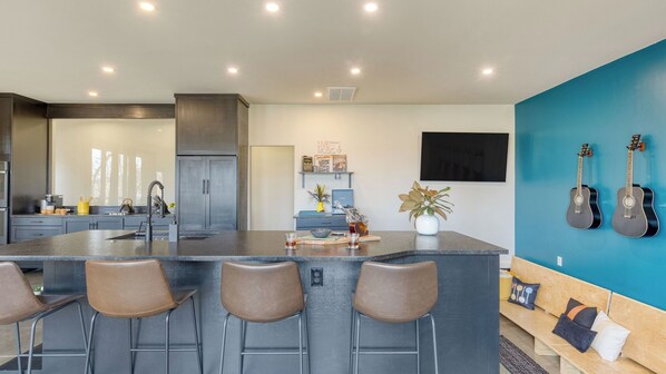Une cuisine moderne dotée d’un îlot central, de tabourets de bar, d’un coin repas avec un banc et d’un mur d’accent bleu.
