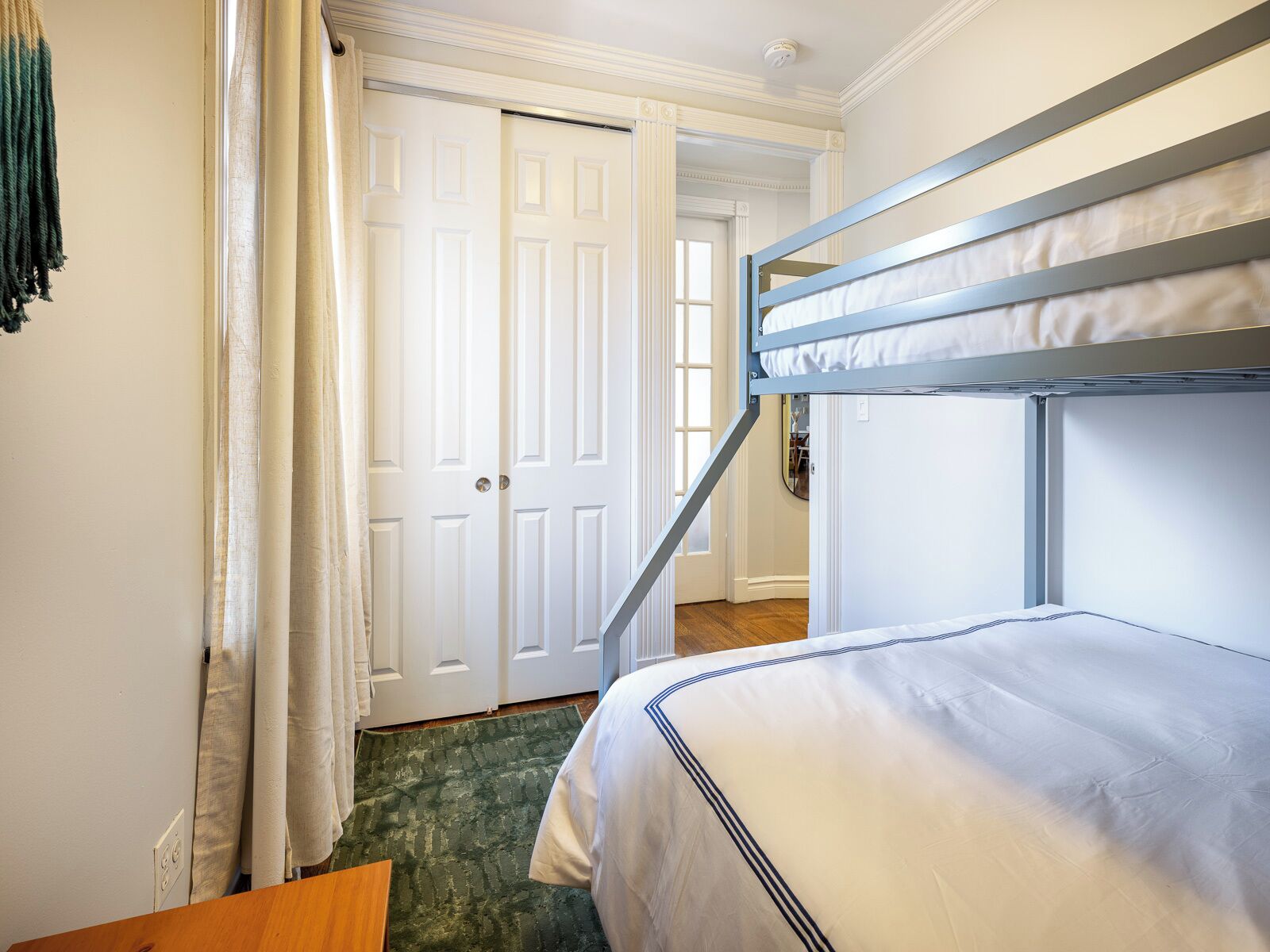 Una habitación con literas, una puerta, una cortina y una alfombra verde.