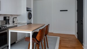 Una cocina moderna con armarios blancos, lavadora integrada, una mesa de madera y dos sillas.