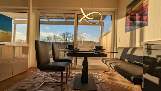 Een moderne keuken met een eethoek, met een groot raam, een eettafel, stoelen, een bank en een vloerkleed.