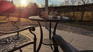Een terras met een gedekte tafel voor thee, stoelen en uitzicht op de zonsondergang.