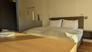 Een slaapkamer met een bed, nachtkastje, spiegel en deur.