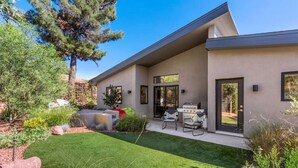 Une maison moderne dotée d’une pelouse bien entretenue, d’un espace extérieur aménagé pour se détendre et d’un barbecue.