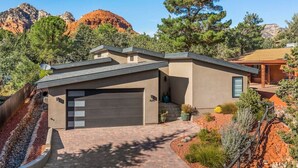 Une maison moderne à deux étages avec un garage, entourée d’un jardin aménagé et de formations rocheuses rouges.