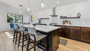 Une cuisine moderne dotée d’un grand îlot central, de tabourets de bar et d’un coin repas offrant une vue sur l’extérieur.