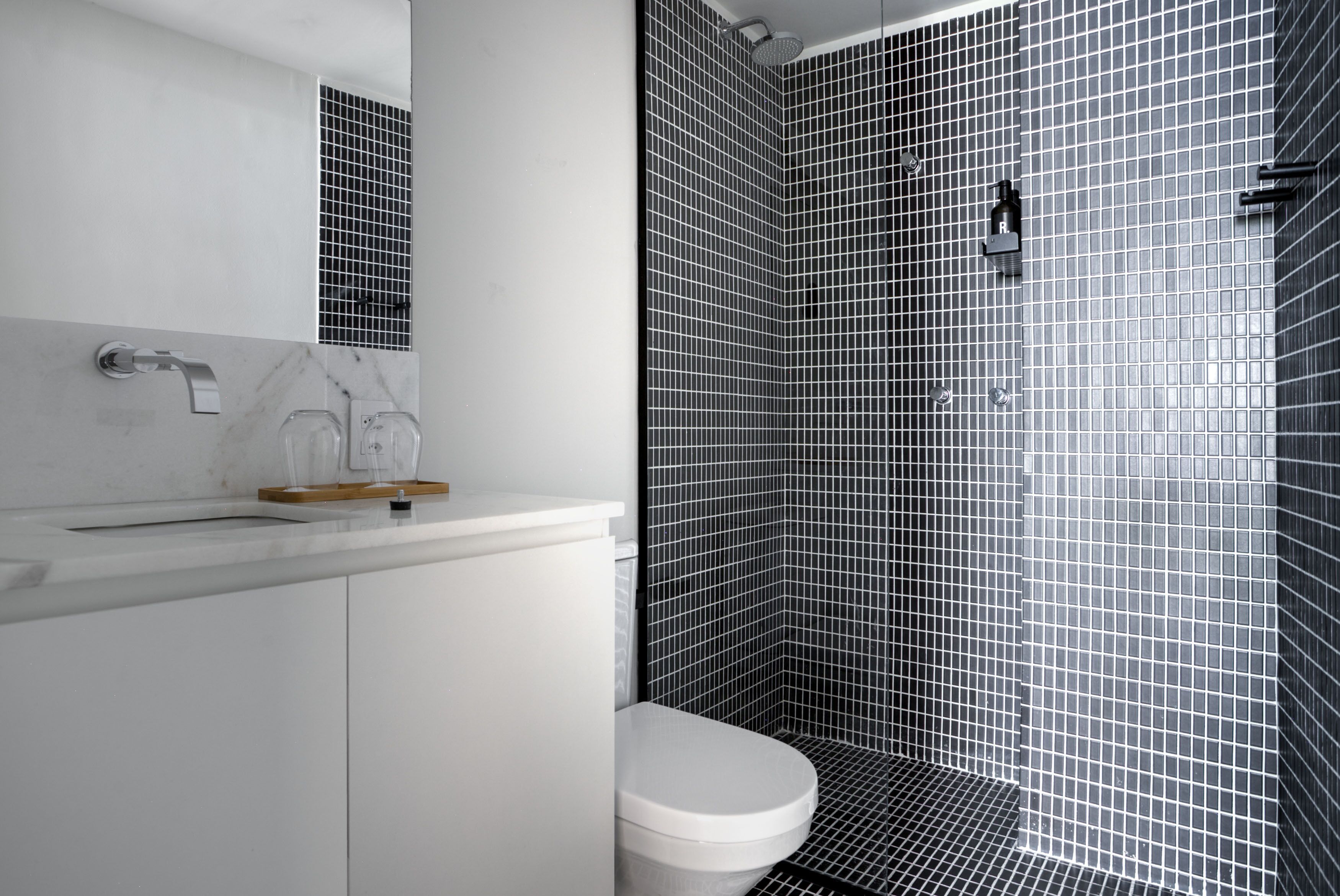 Une salle de bain moderne avec des toilettes blanches, un lavabo agrémenté d’un plateau en bois et un espace douche avec des carreaux noirs et blancs.