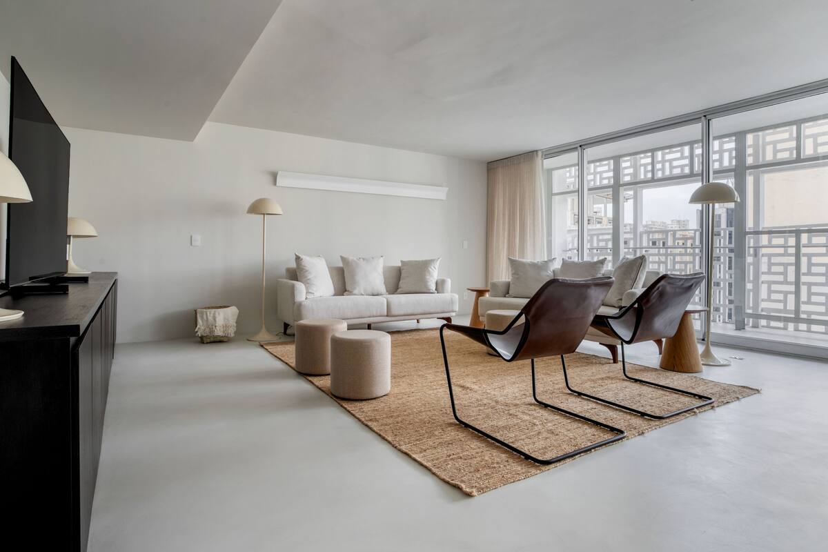 A modern living room with a white sofa, two armchairs, a coffee table, and a large window with a city view.