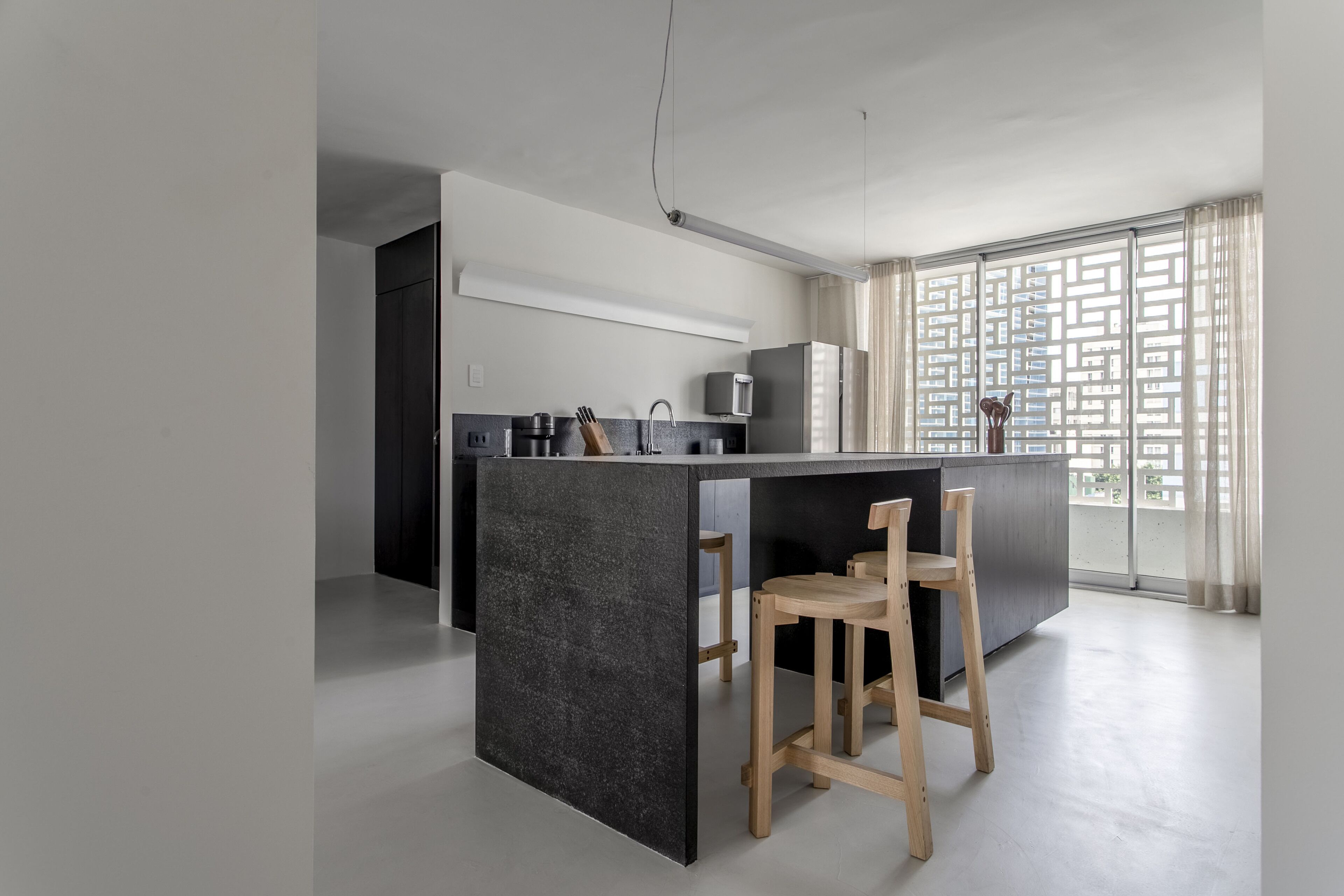 A modern kitchen with a central island, wooden stools, and a large window with a view.