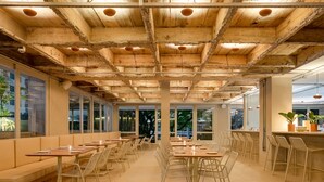 Uma sala de jantar ampla com pé direito alto, grandes janelas e uma variedade de opções de assento, incluindo mesas e bancos.