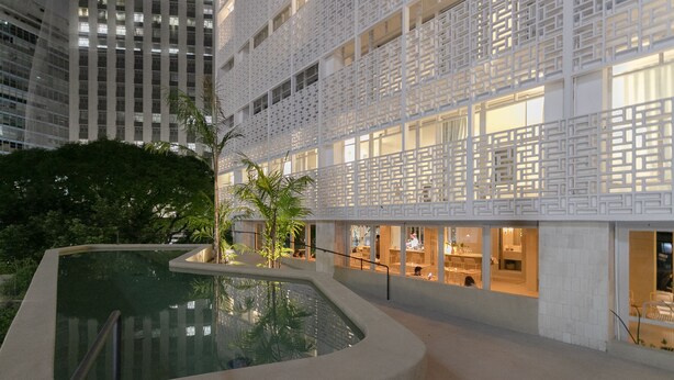 Um átrio interno moderno com piscina central, pé-direito alto e fachada branca geométrica.