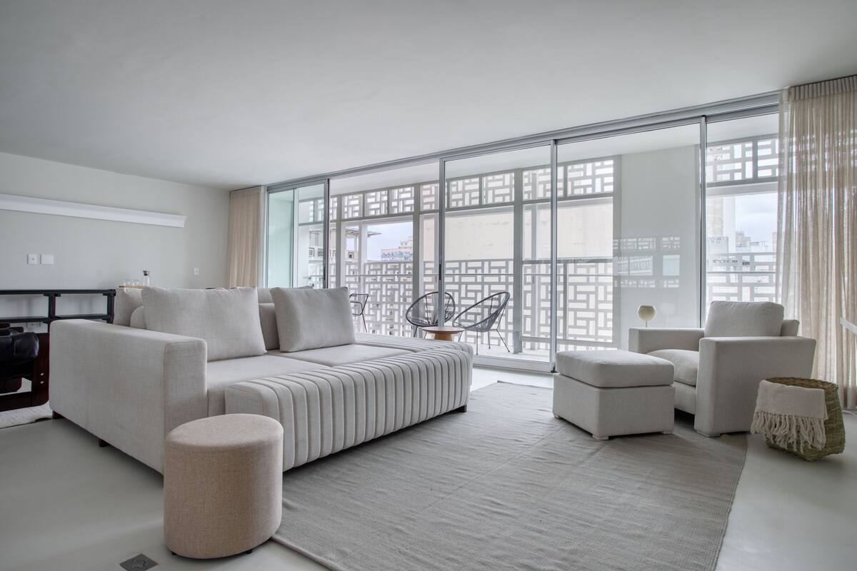 A modern living room with a sofa, ottoman, and chairs, large windows with a city view, and a minimalist design.