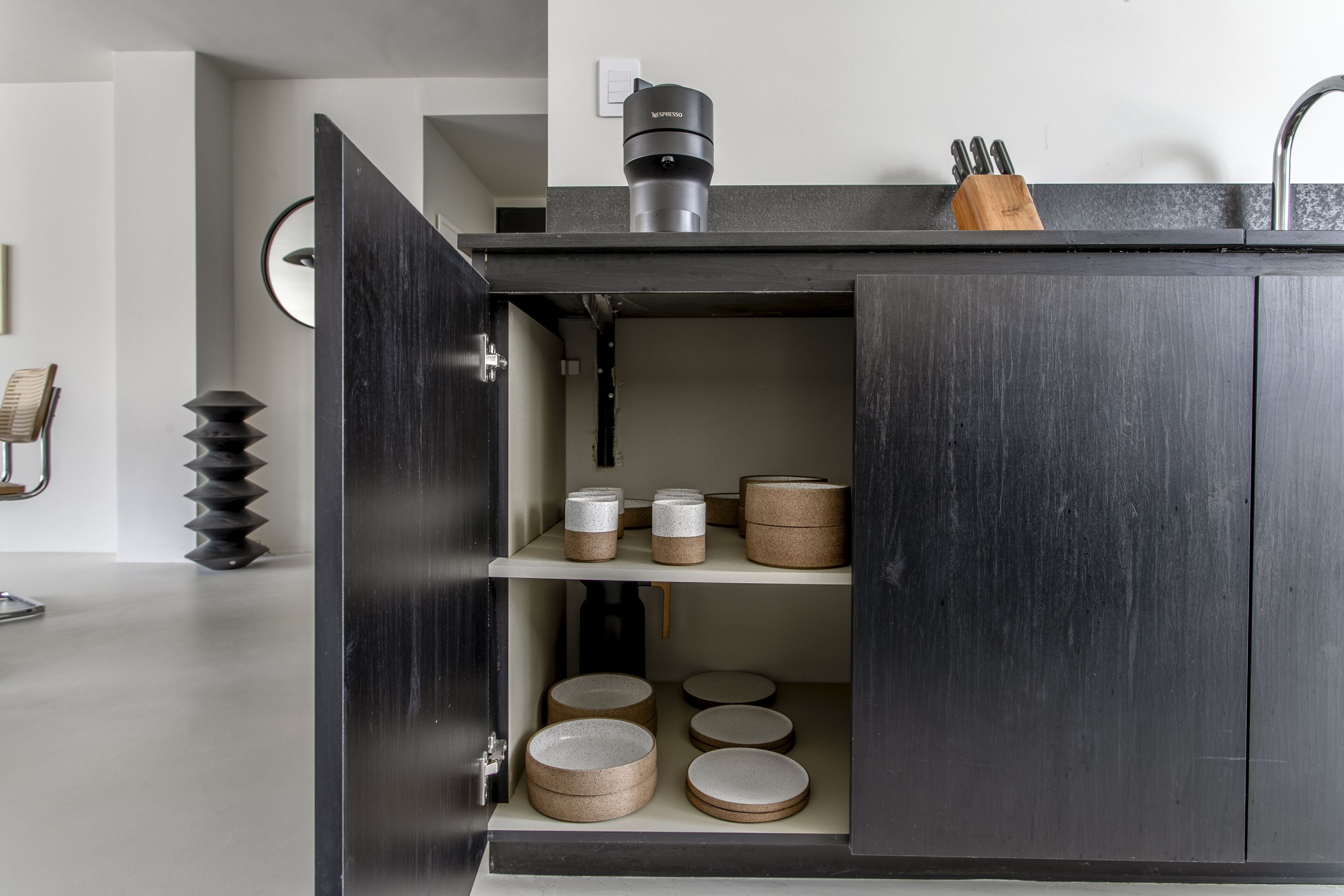 A modern kitchen with a dark wood cabinet, a coffee machine, and various kitchen utensils.