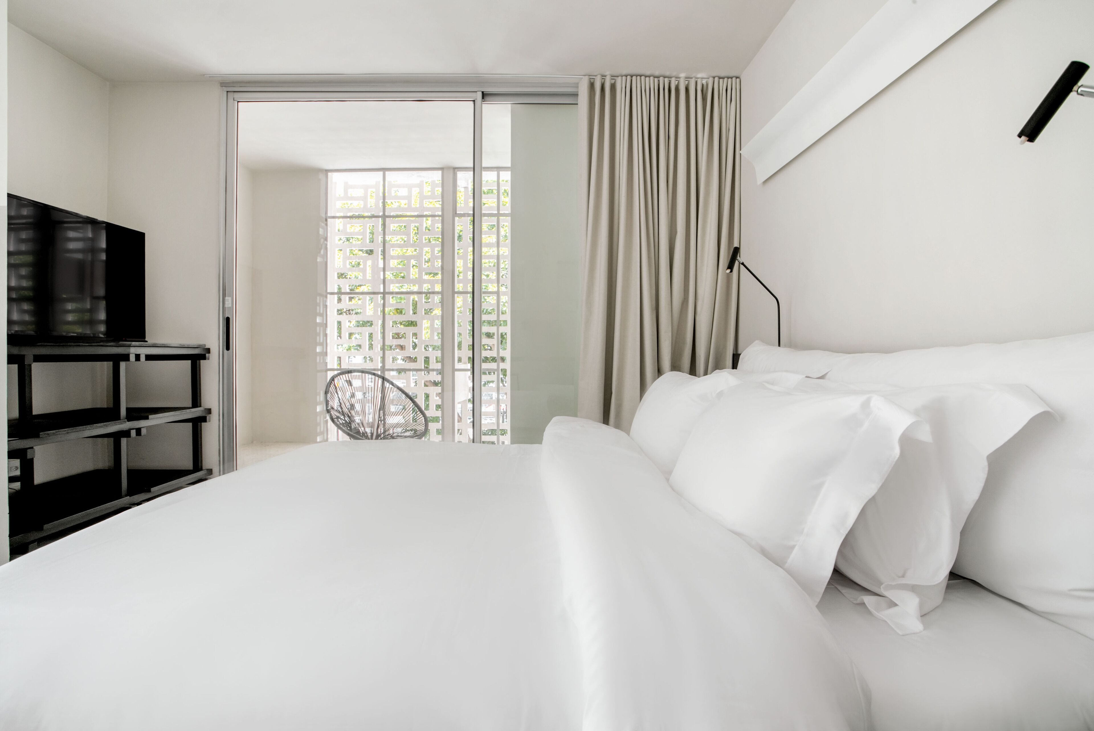 A hotel room with a bed, a TV, a chair, and a view through a glass door.