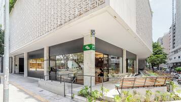 Um edifício moderno com café no andar térreo, mesas ao ar livre e uma placa verde indicando café.