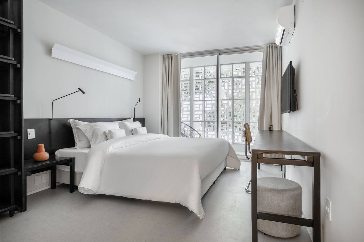 A modern hotel room with a large bed, a desk, and a window with curtains.
