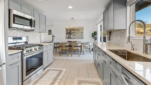 Una cocina moderna con electrodomésticos de acero inoxidable, un comedor con candelabro y vistas al desierto a través de un ventanal.