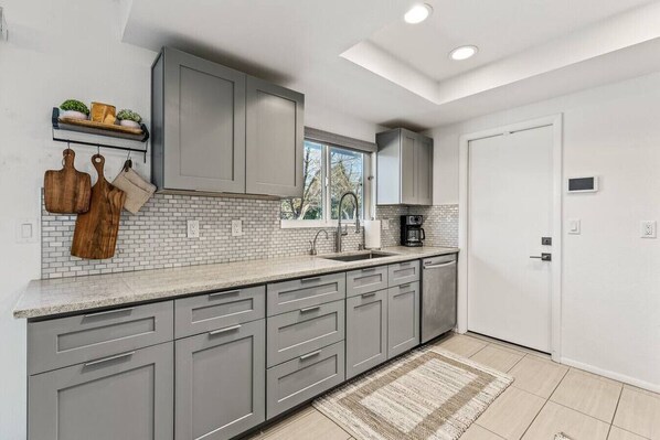 A modern kitchen with grey cabinets, a white backsplash, and a built-in dishwasher.