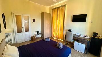 Habitación de hotel con cama, escritorio, silla, cortinas y ventilador de techo.