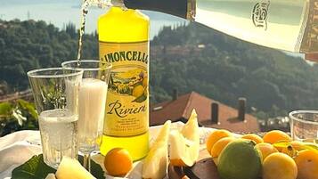 A bottle of Riviere liquor, glasses, and a variety of fruits on a table with a scenic mountain view in the background.