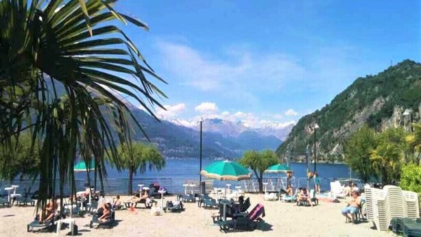 A beach with sun loungers, umbrellas, and a mountainous backdrop. - 2 Rooms in a  wonderful villa, with lake view (Perledo)