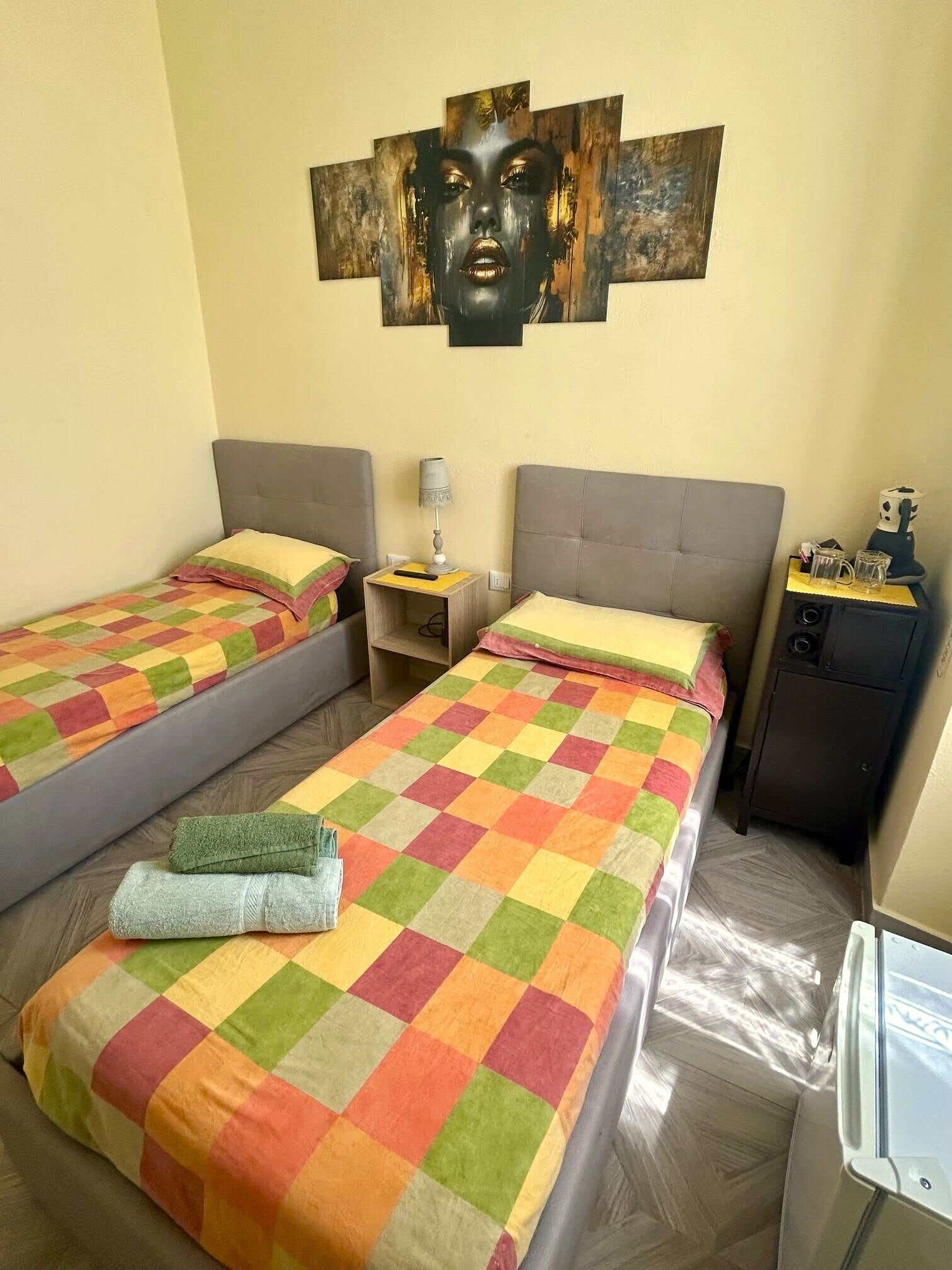 A hotel room with two beds, a small table, a lamp, a cabinet, and a wall art piece.