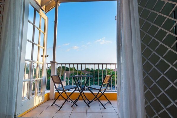 A balcony with a table and chairs, a view of the sky, and a lattice fence.