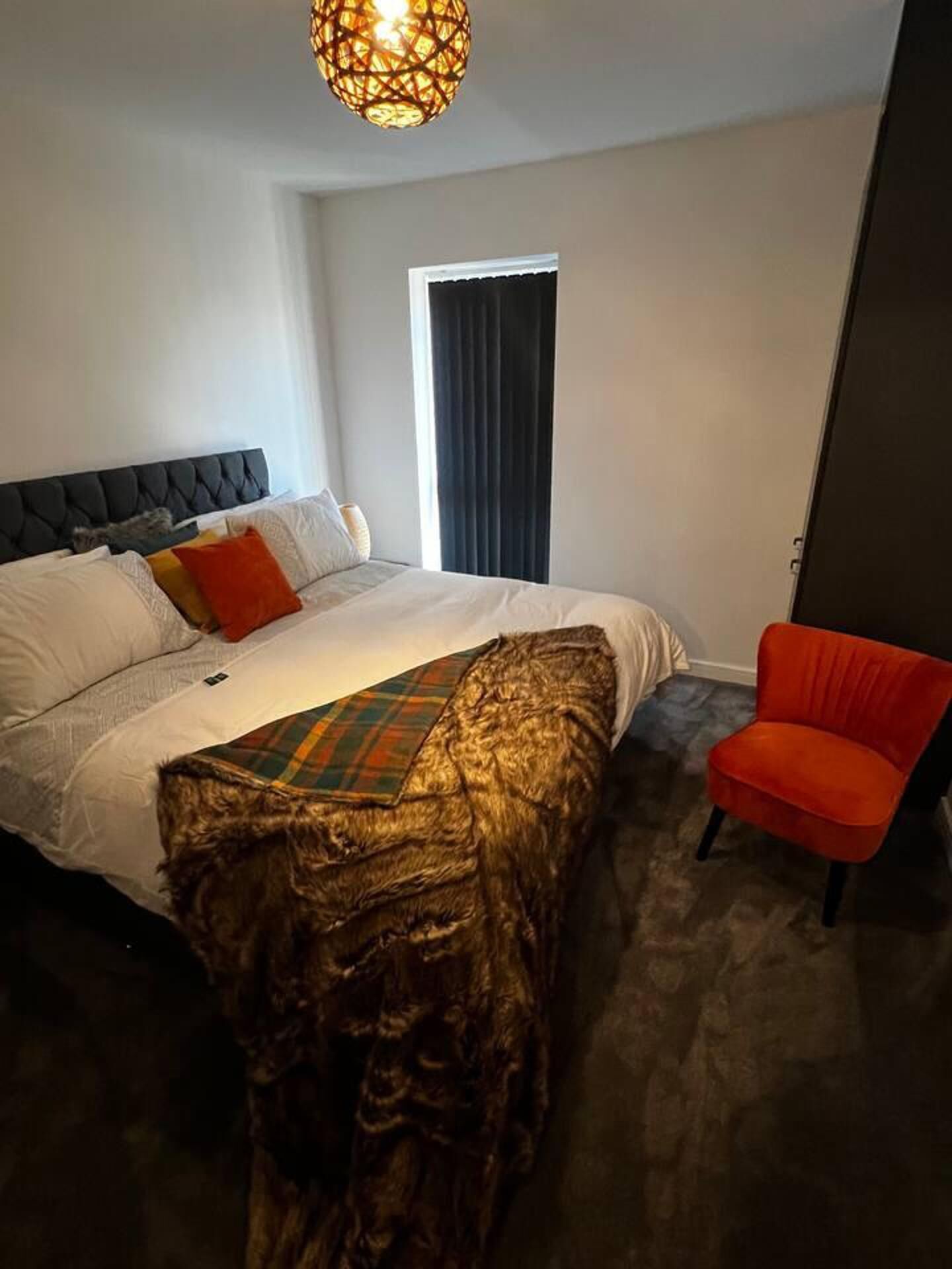 Een slaapkamer met een bed, een rode stoel, een houten hoofdbord en een hangende lamp.